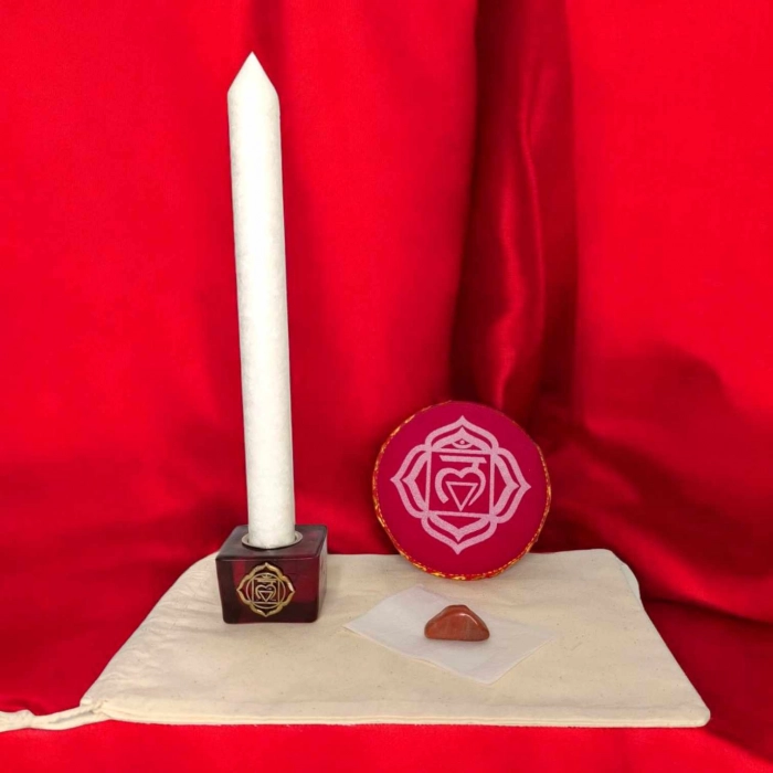Kit rituel énergétique chakra complet avec bougie blanche, coussin rouge, pierre semi-précieuse et bougeoir racine sur fond rouge vibrant.