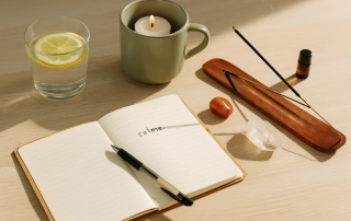 Rituels du matin pour pas péter un câble avant 9h avec carnet de notes, verre d’eau citronnée, bougie, encens, pierres énergétiques et lumière douce sur une table en bois clair. Kit rituel énergétique chakra, affirmations et rituel mantra du matin.
