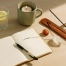 Rituels du matin pour pas péter un câble avant 9h avec carnet de notes, verre d’eau citronnée, bougie, encens, pierres énergétiques et lumière douce sur une table en bois clair. Kit rituel énergétique chakra, affirmations et rituel mantra du matin.